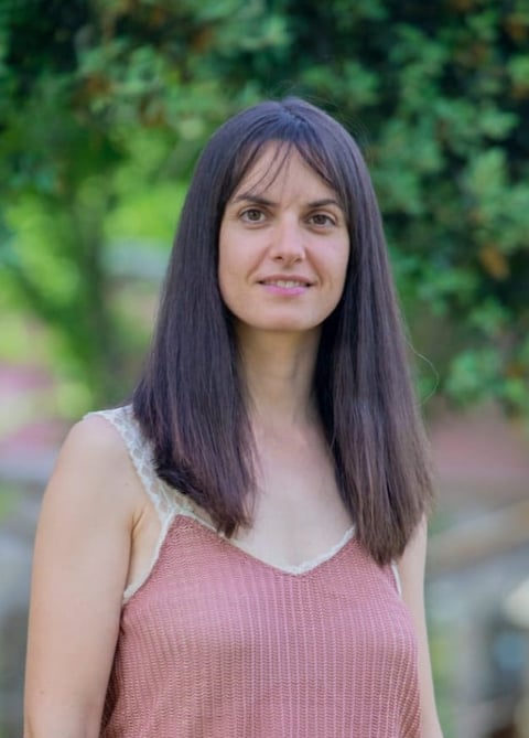 Retrato de mujer con cabello oscuro largo sonriendo al aire libre con fondo de vegetación verde